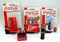 Three Coca-Cola branded magnets in original cards and two loose miniature Coca-Cola bottles on white background. Magnets include vending machine, six-pack of bottles, and ice cold bottle opener designs.
