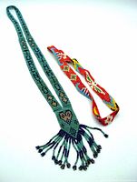 Two vintage seed bead Indigenous handicraft items: a green patterned necklace with beaded fringe and a red stretch headband with eagle and canoe motifs spread out on a white background.