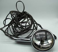 Front view of chrome handheld spotlight with long black coiled cord plugged into car lighter.