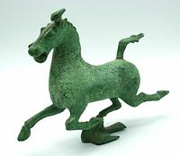 Full side view of the horse statue showing its green patina and dynamic running pose with one hoof on a bird figure.