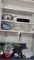Shelves with glass mixing bowls, metal colander, resin colander, and rectangular metal baking pans