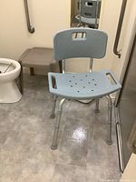 Adjustable shower assist chair with round perforated seat and light blue backrest next to a plastic stool