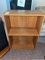 Front view of a medium brown wooden bookcase with two shelves showing interior peg holes for shelf height adjustments.