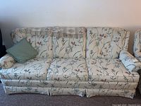 Front view of floral-patterned three-seater sofa with green cushion and blanket on backrest, showing overall condition and wear.