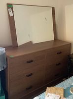 View of laminate dresser with six drawers and attached rectangular mirror on top.