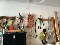 Photo showing wall-mounted tools including extension cords, hedge clippers, and hand saws above a black cabinet