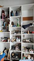 Full view of multiple white shelves filled with assorted home hardware items including bottles, tools, containers, and boxes in a garage setting.