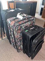 Photo shows the three rolling suitcases lined up, featuring a large black suitcase, a floral patterned medium suitcase, and a smaller black suitcase.