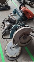 Photo of Makita circular saw with attached blade and two additional saw blades beside it on floor