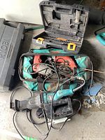 Lot of power tools including Milwaukee drill, Makita reciprocating saw, Black & Decker jigsaw, and a Rona branded black plastic case with drill bits inside