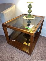 Pair of vintage wood frame side tables with glass tops and lower glass shelves photographed beside a couch, showing the wooden frame construction, glass surfaces, and moderate wear.