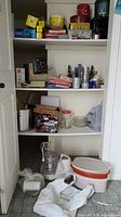 Shelf with kitchen items including cookie tins, plastic containers, glass jars, food wrap, meat slicer, and stock pot