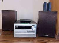 Full view of Panasonic audio system with two matching speakers and remote control on top of central unit.