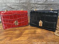 Two mini rectangular fashion bags with crocodile-embossed texture, one red and one black, both with gold lock clasps on a wooden surface.