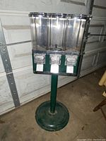 Front view of the 3 slot candy machine on green metal stand showing transparent compartments and coin slots.