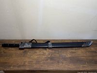 Full length view of Chinese sword sheathed in black scabbard with metal fittings and braided cord