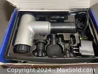 Handheld black muscle massager with four massage heads and power adapter in blue storage box, photo taken to show included parts and condition.