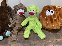 Photo showing brown corduroy plush monkey, lime green plush monkey, and a brown corduroy hippo or bear toy