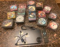 Multiple stacks of DVDs arranged on a countertop with a black Samsung DVD player, a remote control and headphones placed in front.