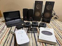 Full view of assorted electronics, includes two Logitech speakers, mini laptop, TP-Link Wi-Fi extender, Suvius wireless charger with box, and three small black security cameras with their chargers.
