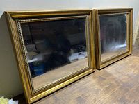 Two matching gold frame mirrors shown side by side on a wooden surface