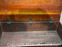 Interior view of the solid wood storage box showing the wooden base and metal hinges that fasten the lid.