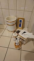 Overview photo showing all ceramic bathroom items together: waste basket, soap dispensers, tissue box, napkin holder, and framed decorative piece