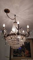 Overall front view of the chandelier illuminated showing six candelabra bulbs, metal frame and beaded crystal tiers