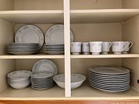 Image of shelf holding stacks of plates, bowls, cups, and saucers with floral pattern and silver trim.