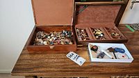 Wide shot showing two jewelry boxes filled with assorted costume jewelry and one smaller box with key chains on a wooden table.