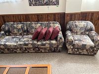 Front view of multicolor abstract patterned sofa with four red throw pillows and matching armchair.