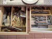 Overview of two kitchen drawers open showing various kitchen tools and cutlery arranged in trays and compartments.