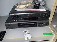 Sony SLV-N50 VHS VCR stacked on top of Zenith DVD/CD player with cables, remotes, and manuals on top.