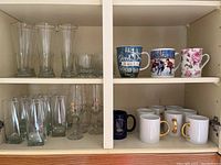 Wide view of the glassware and mugs inside cabinet, showing a variety of glasses and mugs organized on shelves.