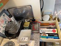 Display of all kitchenware items including baking trays, roaster, strainer basket, rolling pin, parchment paper, tin boxes, and lighter on countertop