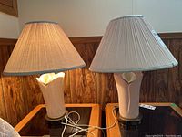 Pair of ceramic and metal base table lamps on wooden table, both with fabric beige lampshades