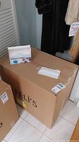 Large cardboard shipping case labeled Feli's with a box of masks and a single white disposable earloop mask on top.