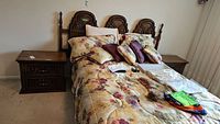 Pair of vintage wooden night tables positioned beside a bed with floral bedding. Both tables are identical with matching wood tone and design.
