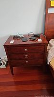 Front view of a wooden night table with three closed drawers and metal square knobs.