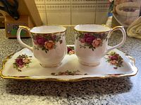 A view of the server plate with two Old Country Roses tea cups placed on it, showing floral pattern and scalloped gold edges.