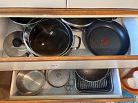 Two drawers with multiple pots, fry pans, covered pot, graters, metal bowls, and bakeware molds showing the variety of items in the lot.