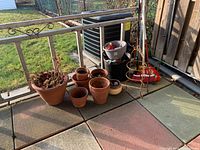 Outdoor patio with multiple clay and plastic pots arranged on ground near railing along with broom handles visible.