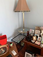 Magazine rack with glass top and metal frame next to metal and glass table lamp with beige cloth lampshade.