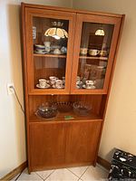 Front view of teak corner china cabinet showing glass-front upper doors and lower storage compartment.