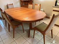 Six teak dining chairs surrounding a teak dining table, all with beige upholstered seats and backs
