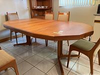 Full view of the teak dining table with two leaves installed, showing the continuity of the wood grain and the shape of the table.