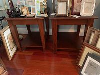 Two wood side tables placed side by side with picture frames and other decorative items on top and around them.