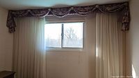 Full view of window with two cream curtains and floral valance above.