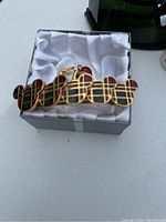 Gold-tone metal hair clip featuring multiple Mickey Mouse head shapes in red and black plaid enamel design, resting in white fabric inside a box.