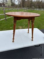 Front angle view of rock maple end table showing round tabletop and turned legs.